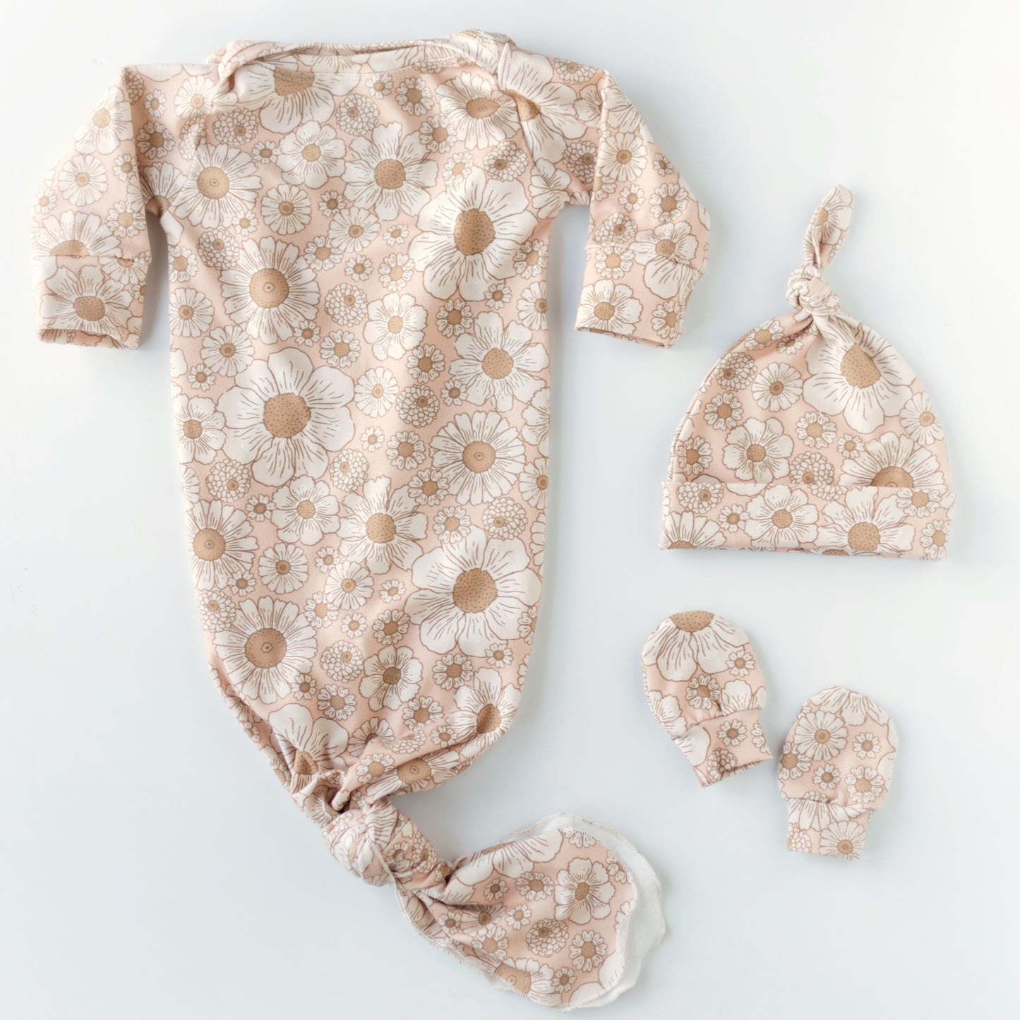 A light pink baby knotted gown with floral patterns, accompanied by a matching hat and no-scratch mittens, set against a white background.