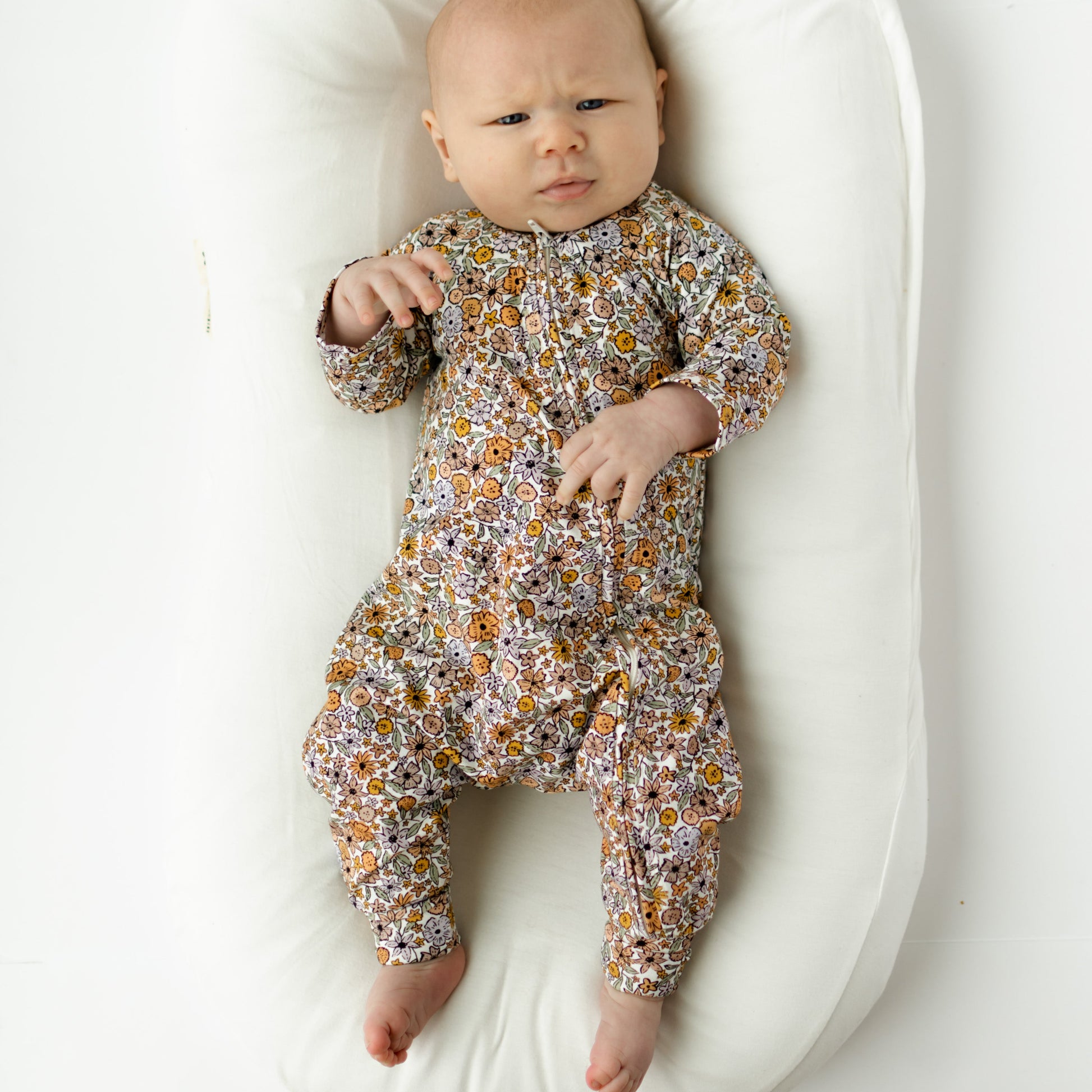 Baby in a floral onesie lying on a white cushion