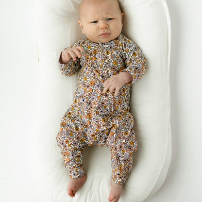 Baby in a floral onesie lying on a white cushion