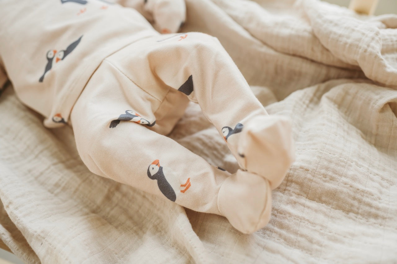 Baby legs in beige pants with bird designs on a soft beige blanket