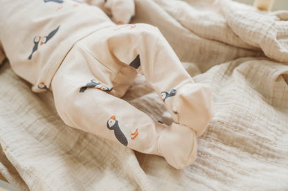 Baby legs in beige pants with bird designs on a soft beige blanket